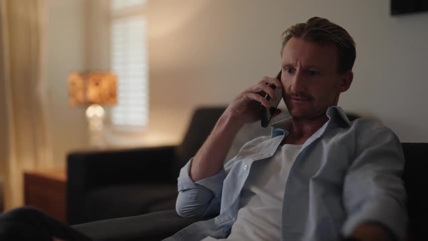A man uses a remote to turn off his television while talking on the phone