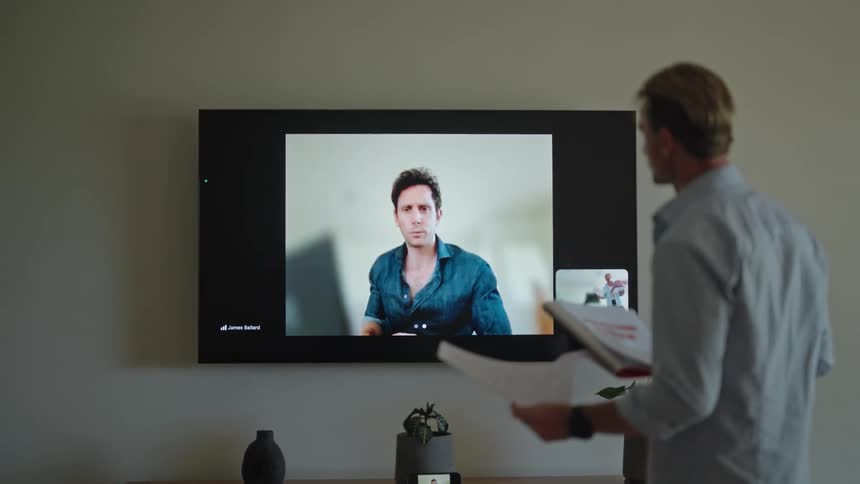 Two men video chatting via a television one with papers in his hand