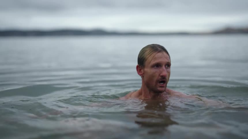 A man is swimming in the lake and he bounces underwater and comes back up and swims away