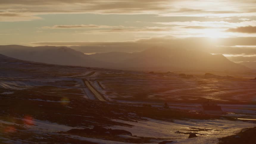 Aerial view of the sun setting behind clouds over the distant mountains at evening