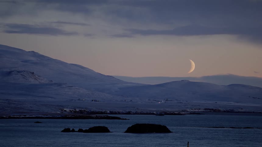 Landscape of distant village on mountain slope and waning crescent moon