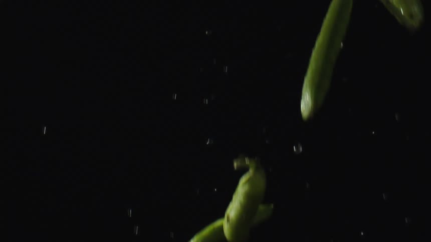 Wet green pods thrown into air against a black background fall again