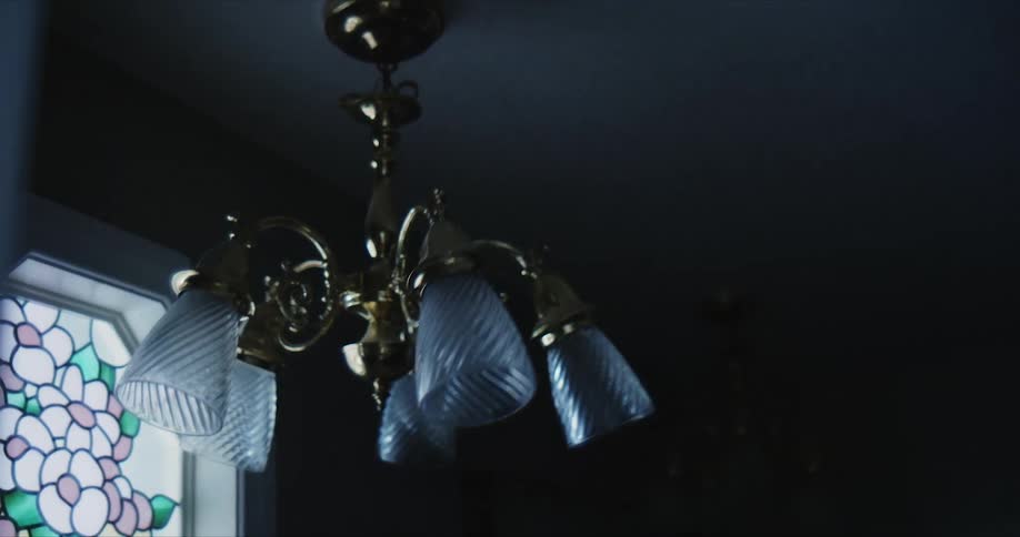 Golden ceiling light fixture swings near a stained glass window