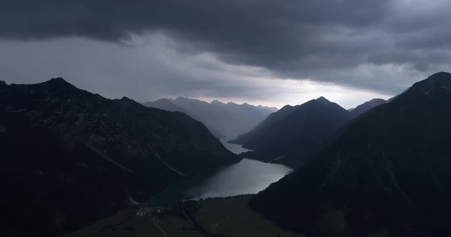 Aerial view of high mountains and lake being silhouetted against the cloudy sky