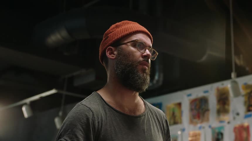Close up of the face of a bearded man wearing a beanie standing on the halls of a museum