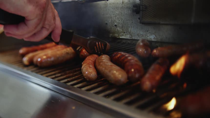 A person is grilling hot dogs outdoors on a grill