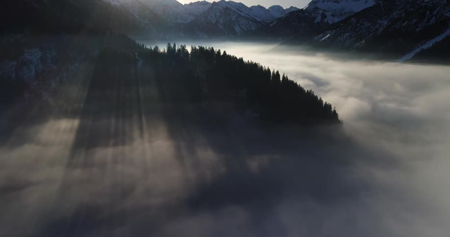 An aerial of mountains trees and fog setting over water at dawn