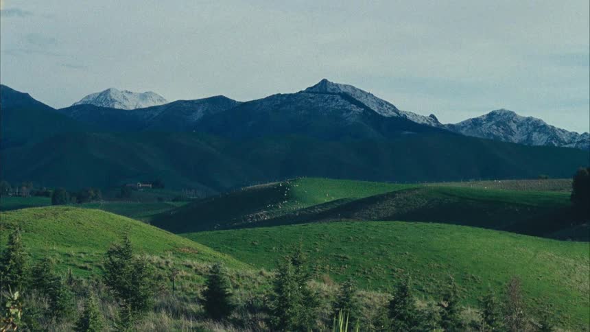 A wide shot of a hilly grassy landscape with snowy mountains in the distance
