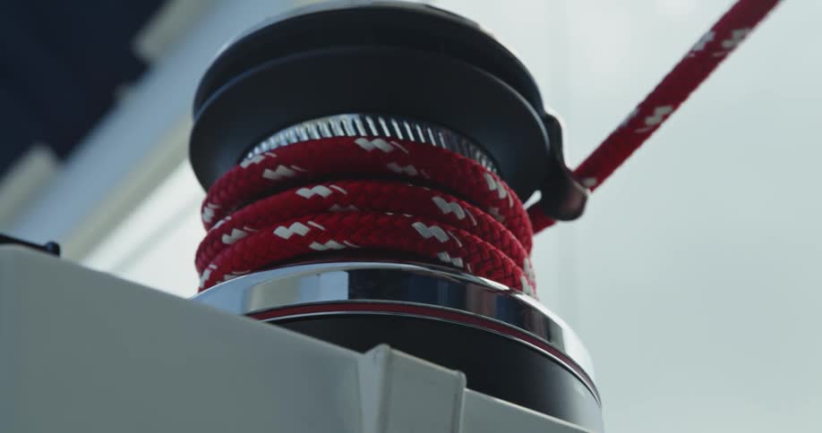 Close up of the hands of a man tying a red rope around a boat cleat