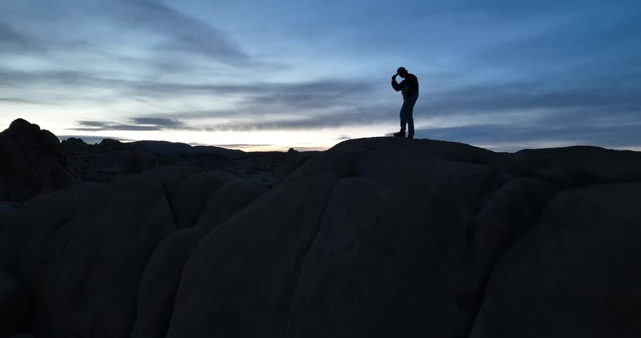 Silhouette of a person standing on a mountain as they move the cap on their head with their hand