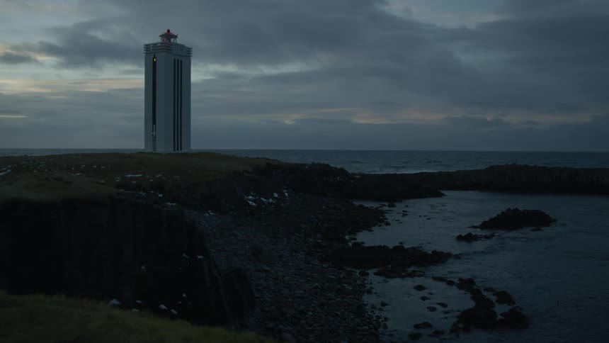 A lighthouse on a coastline at dusk against a grey cloudy sky