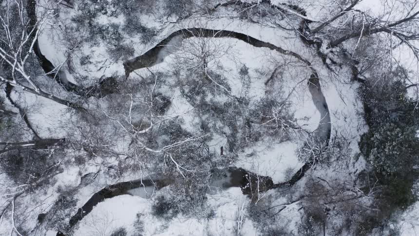 Top down aerial view of a river turning and twisting on a landscape covered in snow