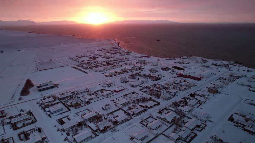 An aerial view of the sun setting over a snowy coastal community