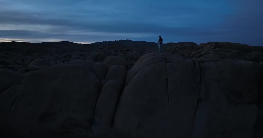 A person is standing on the top of a mountain under a dark blue cloudy sky