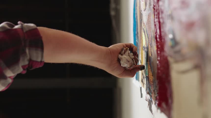 Artist rubs paint covered finger on artwork hanging on wall