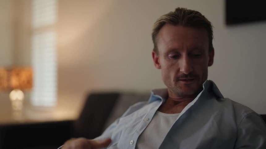 Man sitting on couch finishes call on smartphone turns the tv on