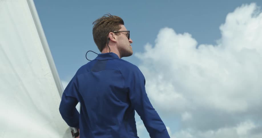Young man with clothes waving on the wind stands on a sailboat looking at the horizon
