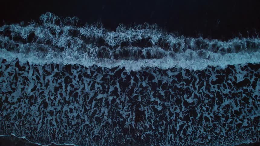 Top down aerial view of waves gently crashing on the coast at evening