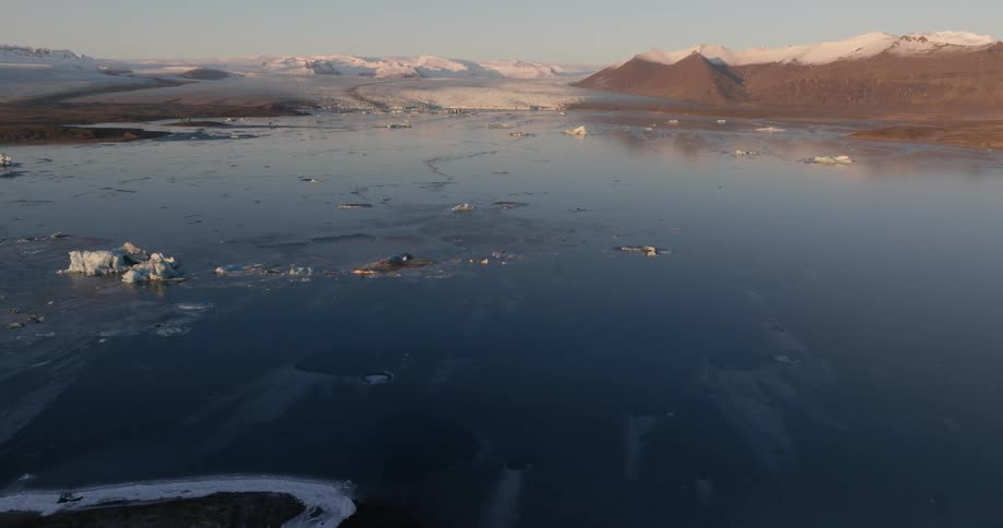 Aerial view of pieces of ice floating on the ocean in front of a glacier at evening