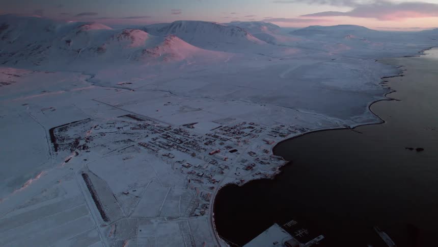 An aerial view of snow covered lands and a rural town along the coastline