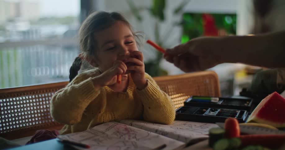 Father feeds his daughter pieces of carrot while cooking at home