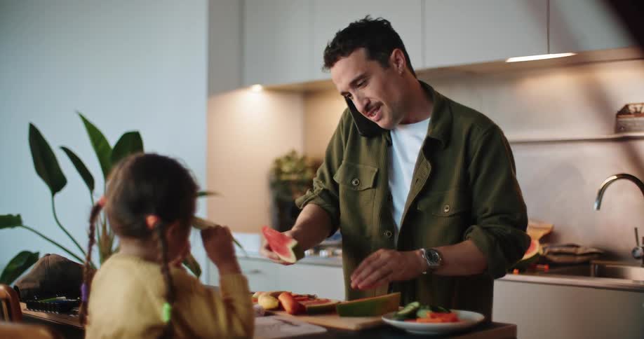 Man talking on the phone while preparing a meal for his daughter at home