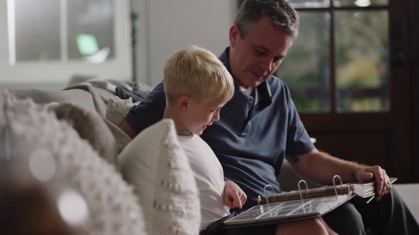 Grandfather sits on couch showing his grandson a photo album