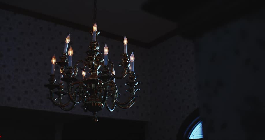 A chandelier with the lights on sways in a dark room