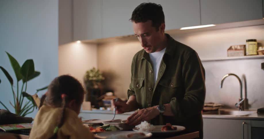 A man preparing food and plating it in front of his daughter in the kitchen