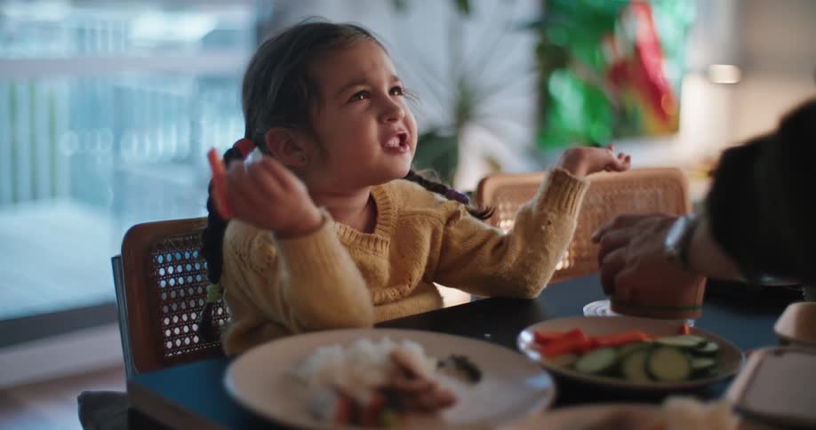 A little girl eating moving her hands while talking to the person in front of her