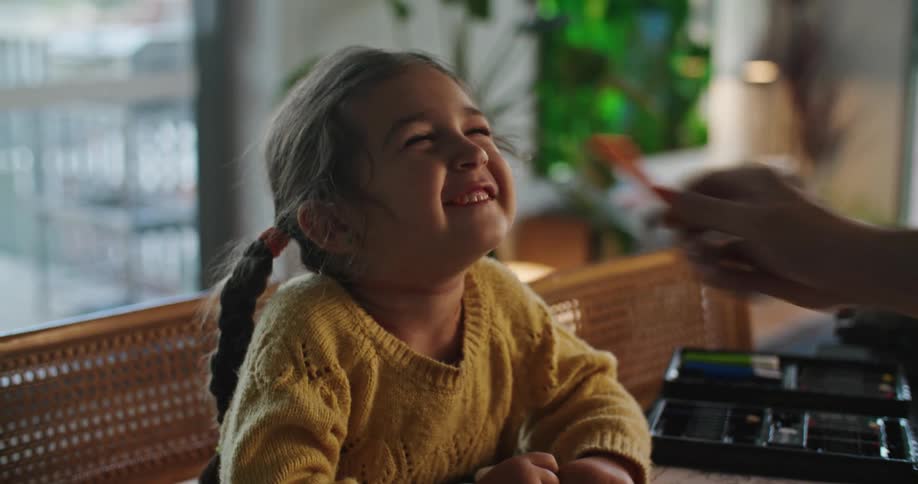 Father teases girl as she draws at dining table