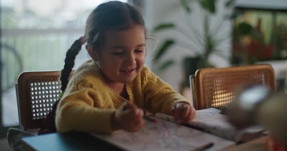 Little girl in yellow sweater scribbling with crayon in coloring book