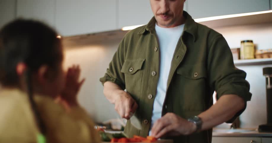 Father slices vegetables in the kitchen while talking to daughter