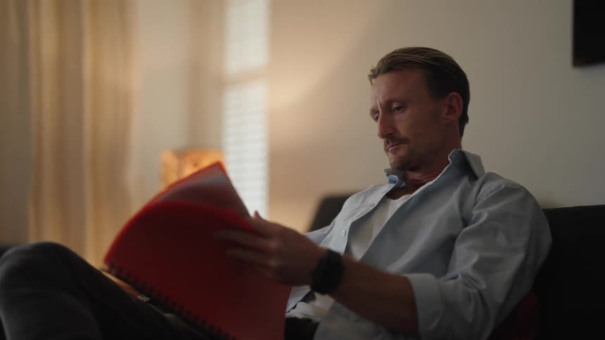 A man is sitting on a couch and reading papers