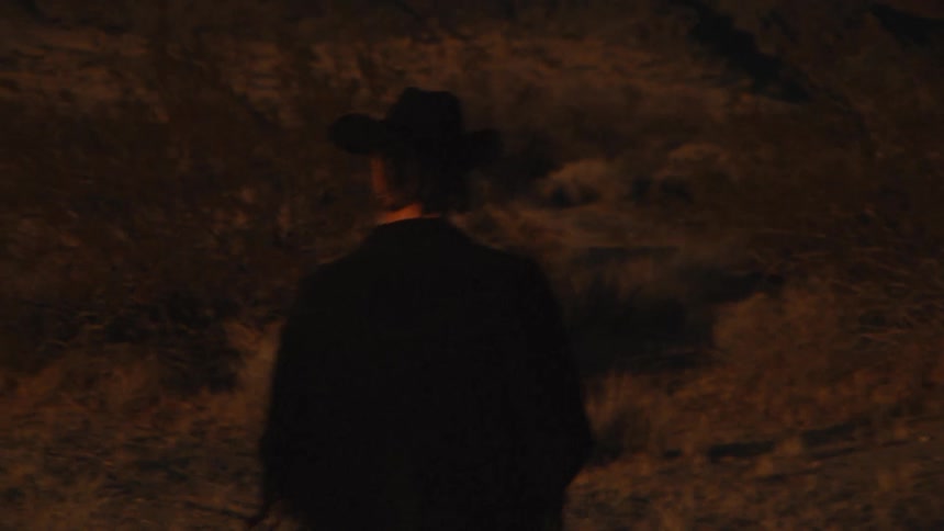 Man walking in the night with dressed like a cowboy and moving around in the farm land