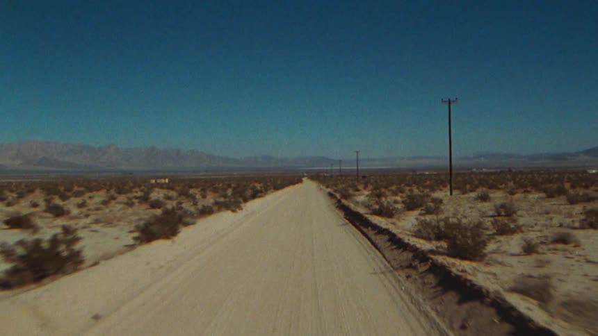 The point of view of someone riding something down the street is shown with a blue sky and mountains in the background