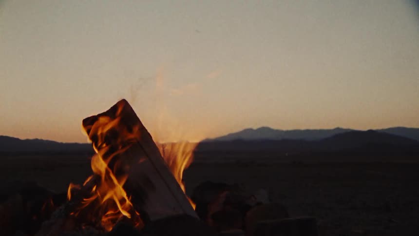 Flames and smoke rise from a burning bonfire and there are mountains in the distance