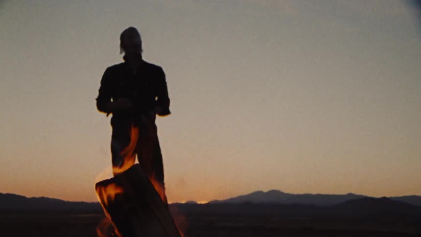 A silhouette of a man standing near a fire putting a cigarette in his mouth
