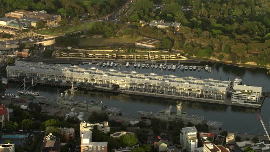 An aerial orbiting view of a ship port with large navy ships docked