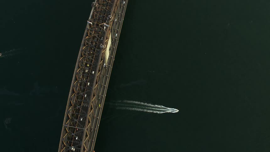 Birds eye view of boat cruising under a steel bridge in the harbor