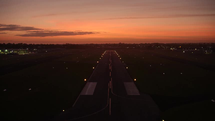 An airport runway lit up at dusk as the horizon is lit up orange at dusk