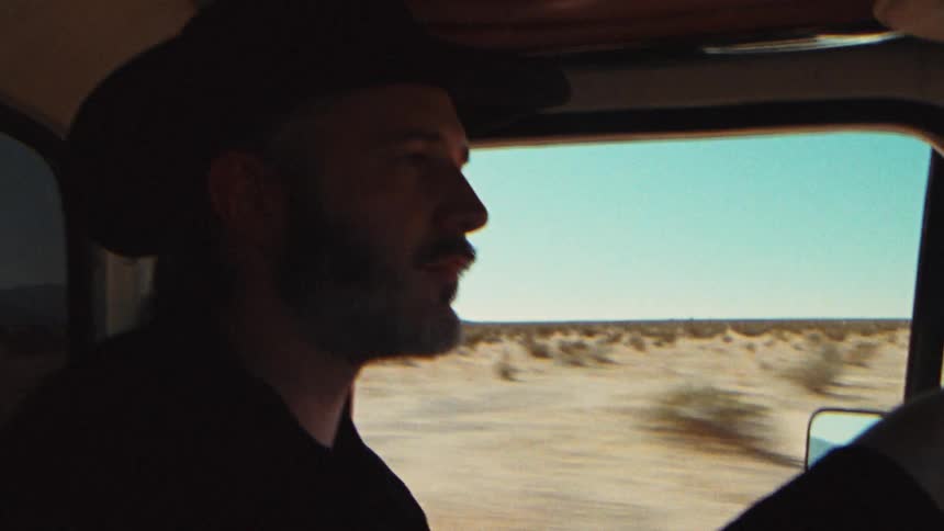 A cowboy with his hat driving through a desert
