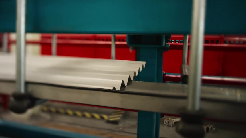 Large piece of white corrugated metal moving down conveyor belt in factory