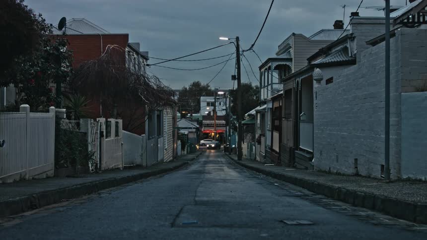 Car with headlights on drives on a narrow street between houses in a small town at morning