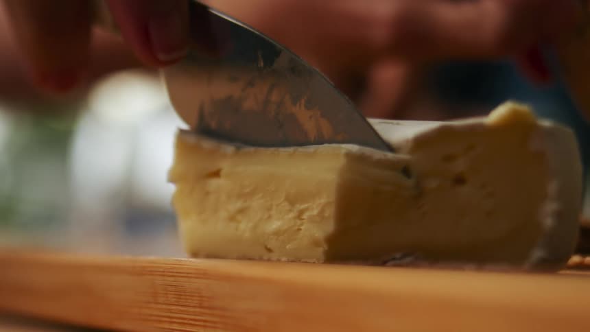 Close up of a person using a knife to cut a slice of soft cheese