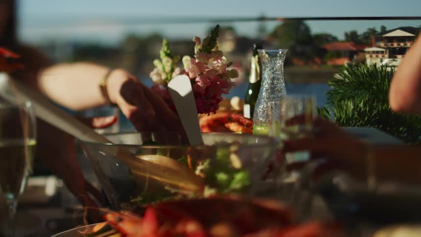 A table full of food and drinks with people reaching for bowls and glasses