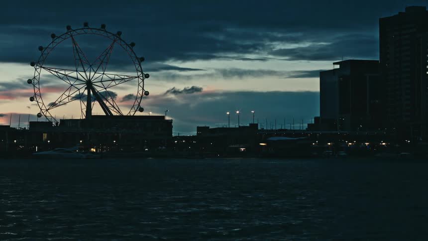 Silhouette of a ferris wheel in a waterfront city at nightfall