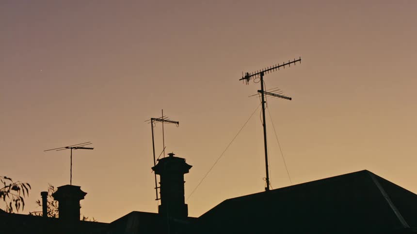 Antennas on building roofs are silhouetted against the sky at sunset
