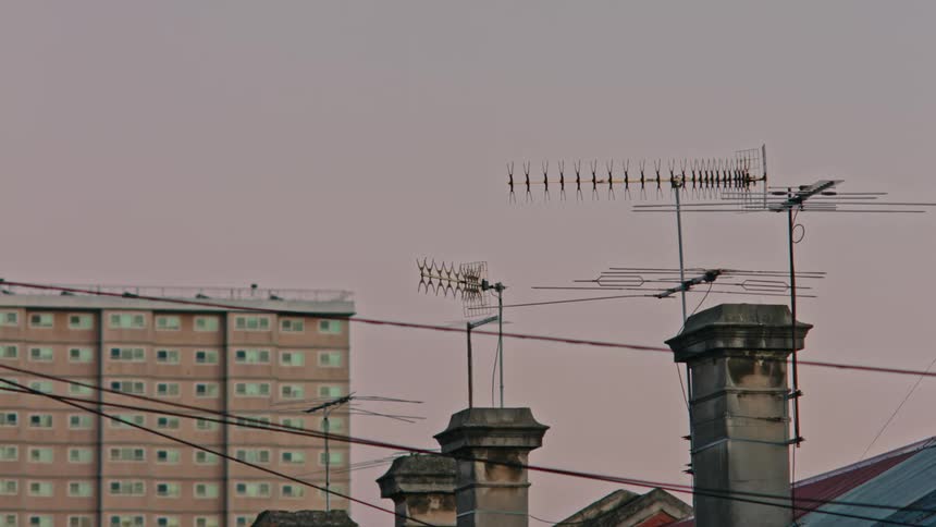 Homes with antennas mounted to chimneys with a large apartment building in the background at dusk