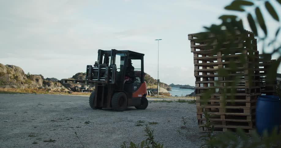 Man driving a forklift on a yard picks up a wooden pallet